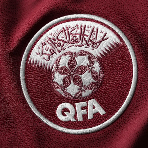 Qatar football crest on maroon jersey fabric background